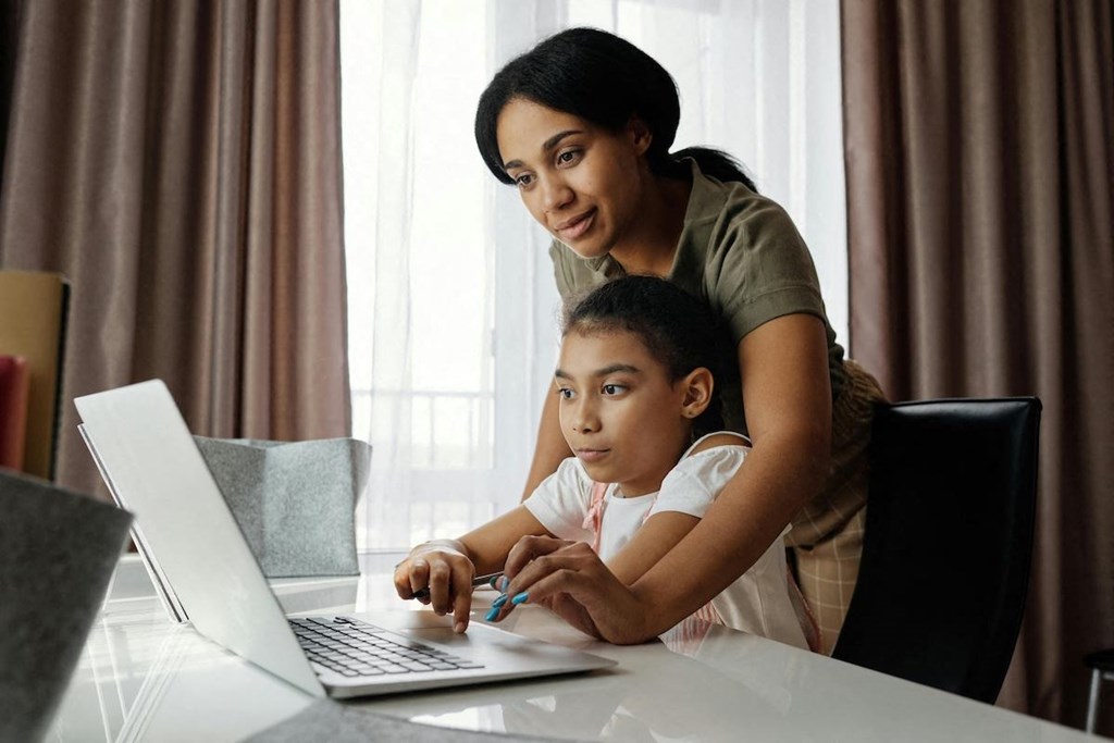 a woman and a child looking at a laptop computer in front of a window
