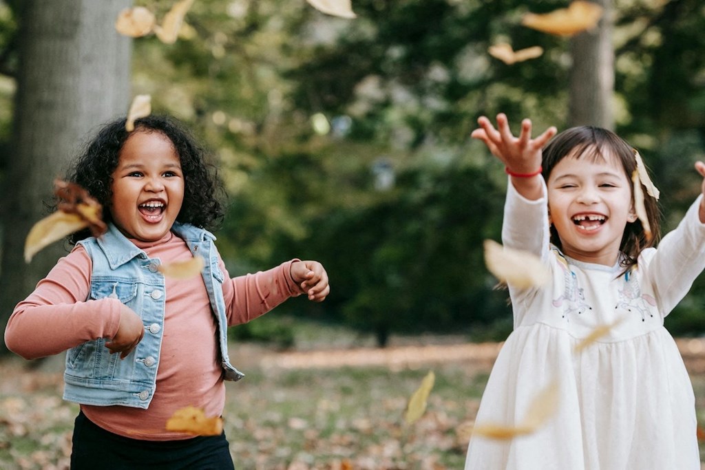 two young girls playing outside and tossing autumn leaves in the air