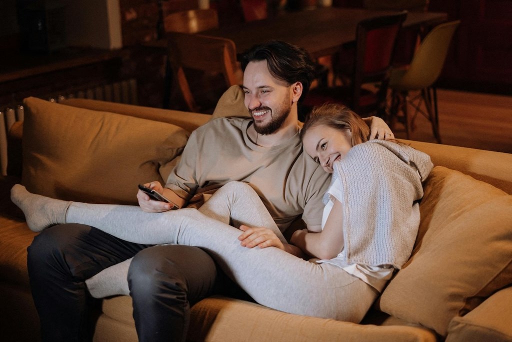 a man with a tv remote in his hand and woman sitting on a couch