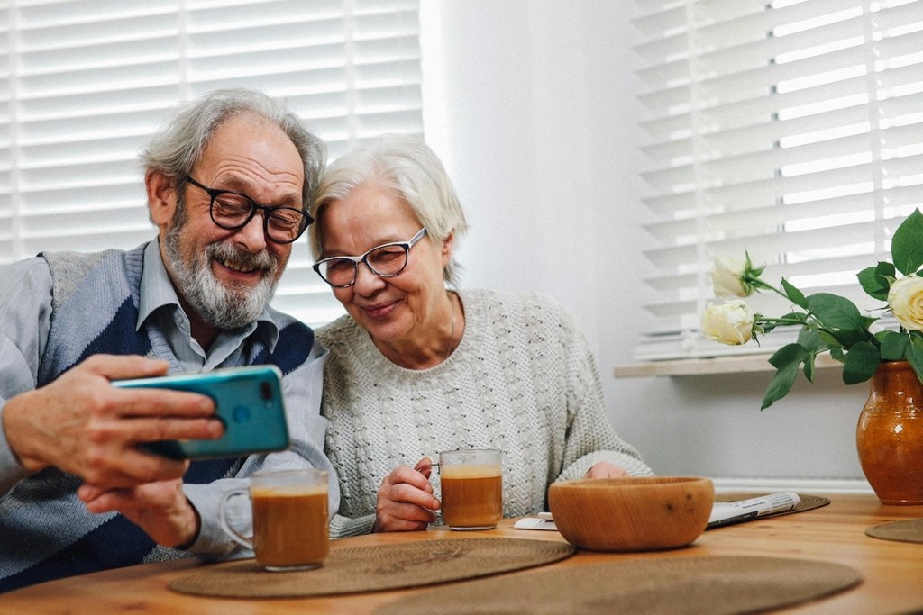 an older man and woman looking at a cell phone and sitting at a table