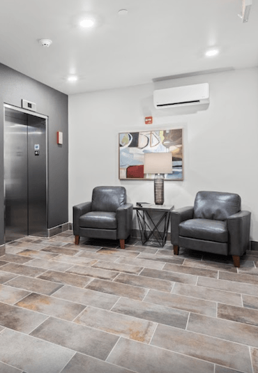 two chairs and a table with a lamp in front of the elevator bays at River Flats Apartments