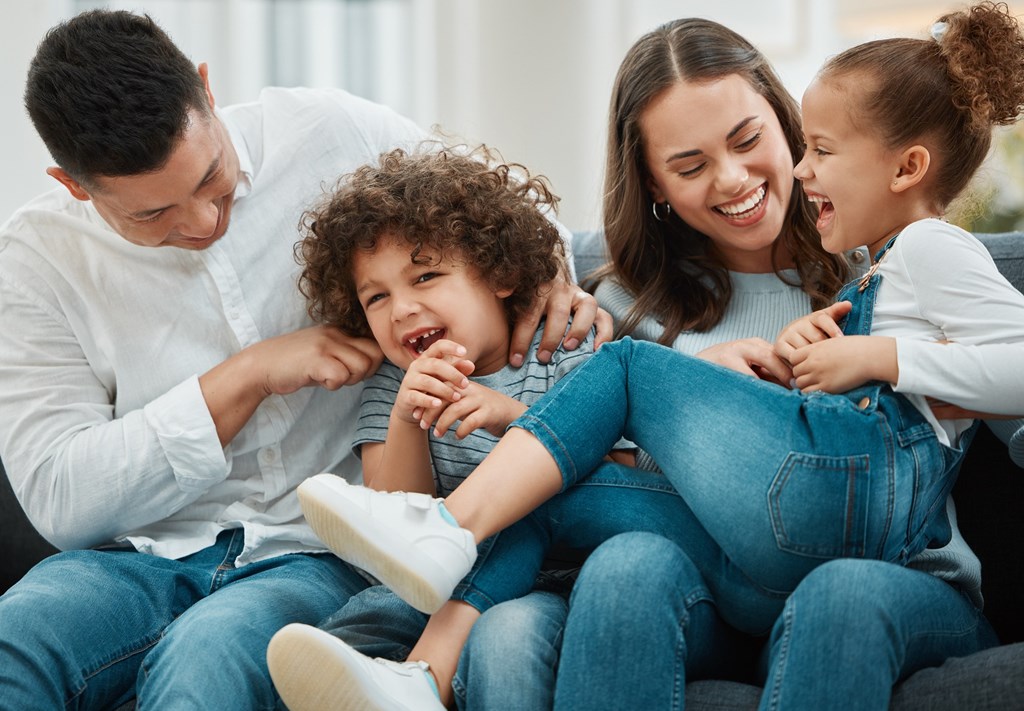 A family of four is sitting together on a couch, sharing a joyful moment.