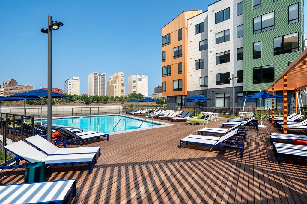 a swimming pool with chaise lounge chairs and umbrellas in front of an apartment building