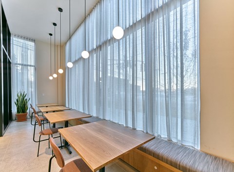 a dining room with long wooden tables and chairs and windows with white curtains