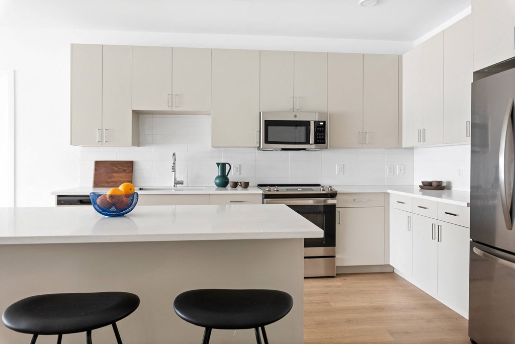 a kitchen with white cabinets and a large island with black chairs