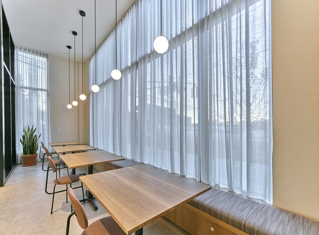 a dining room with long wooden tables and chairs and windows with white curtains