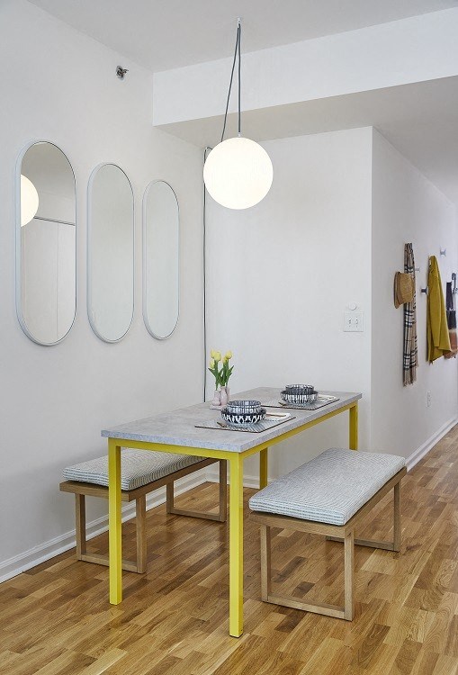 a small dining room with a yellow table and two mirrors on the wall