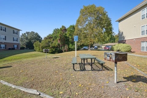 A picnic table is in the middle of a grassy area with a sign in the background.
