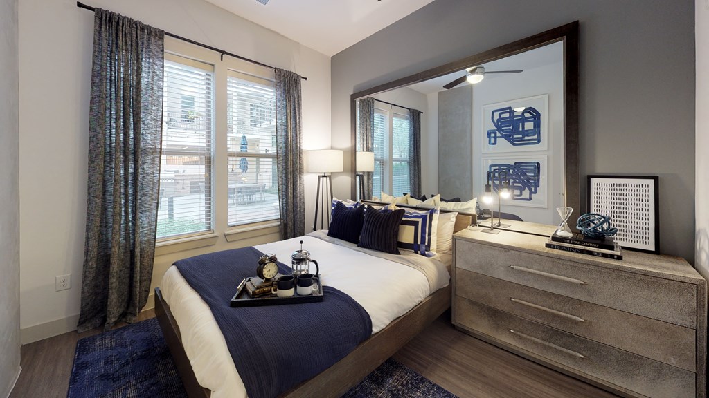 Bedroom with wood flooring, a bed, and dresser next to a window