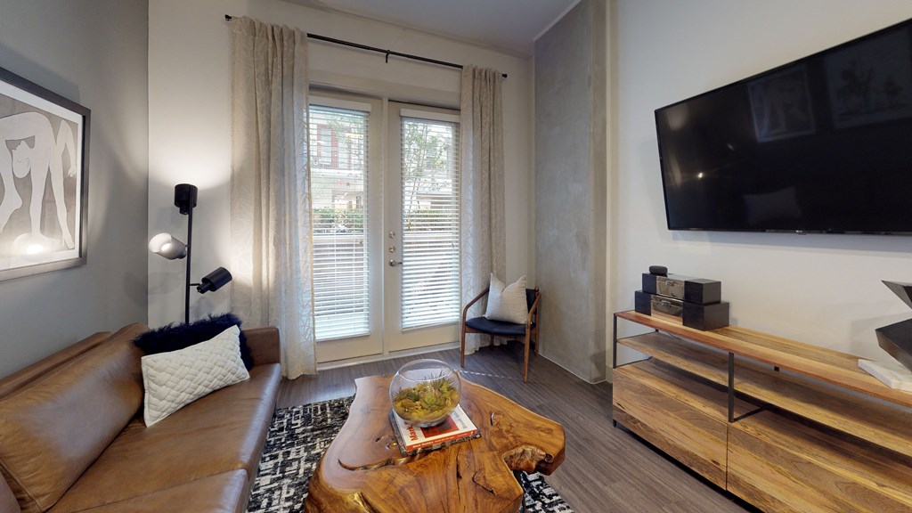 Living room area facing a couch next to an exterior window next to the kitchen