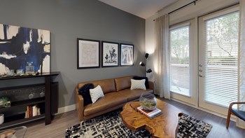 Interior of one bedroom model living room facing couch and bookshelf next to exterior patio door - Photo Gallery 120