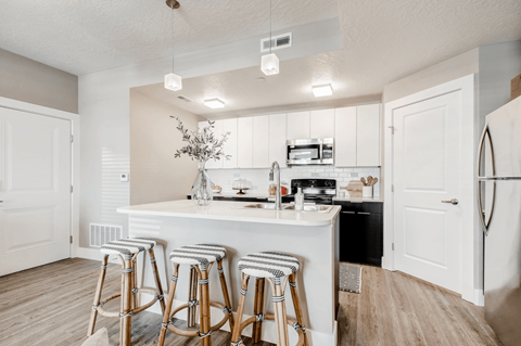 A kitchen with white cabinets and a white island with bar stools.