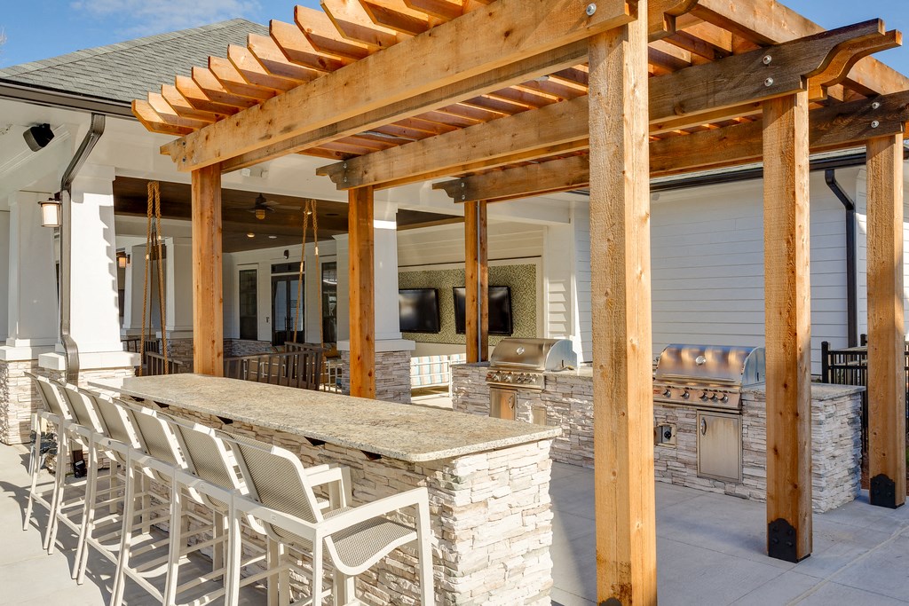 a patio with a bar and chairs under a wooden structure
