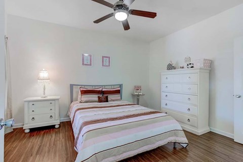 A bedroom with a bed, dresser, and ceiling fan.