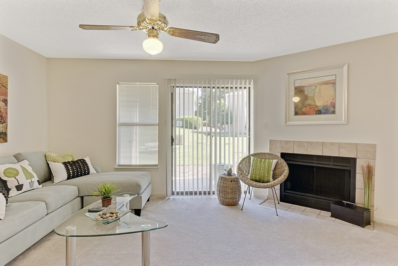 A living room with a grey couch, a glass table, a chair, a fireplace, and a painting on the wall.