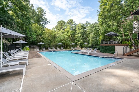 A large outdoor swimming pool surrounded by trees and lounge chairs.
