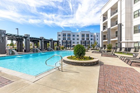 A swimming pool surrounded by a brick walkway and a small garden in the middle of a residential area.