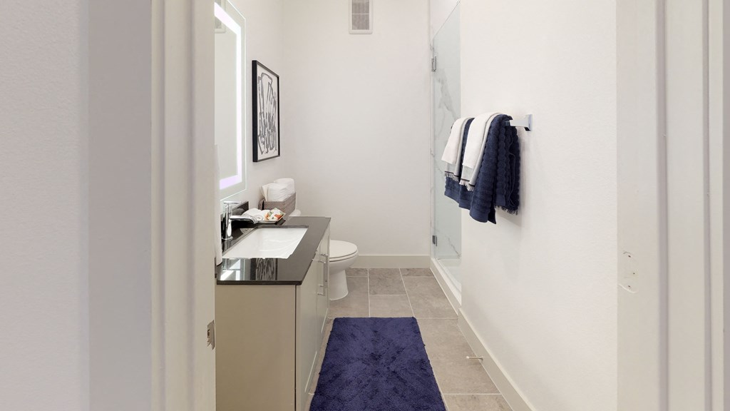 Bathroom facing sink with cabinets underneath, toilet and shower
