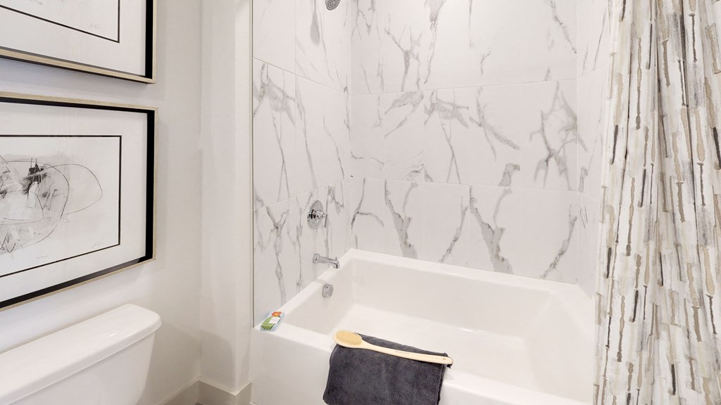 Bathroom facing large bathtub with marbled tile, brushed nickel hardware, and a towel hanging from the side of the tub.