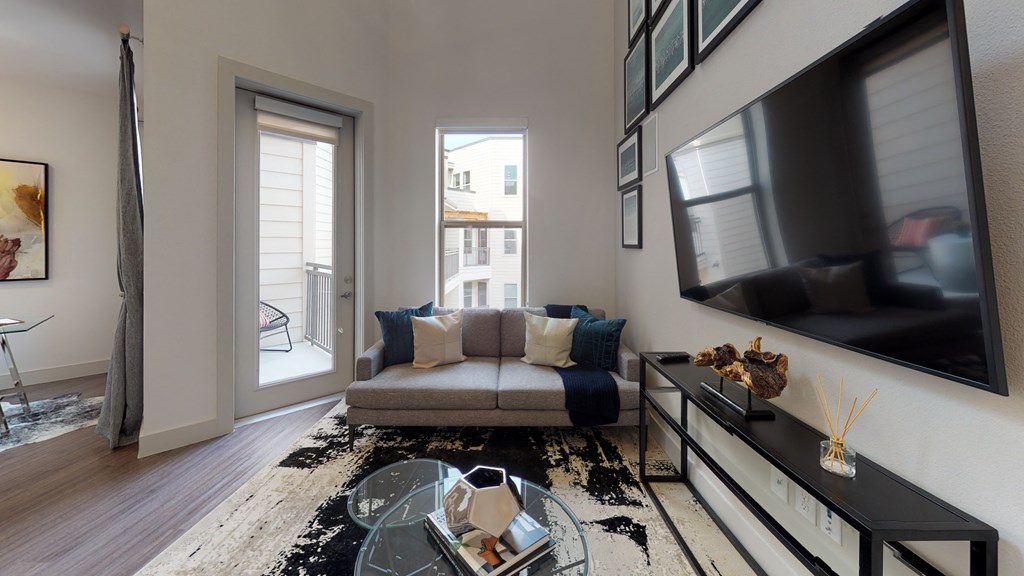 Living room area facing a couch next to an exterior window next to the kitchen