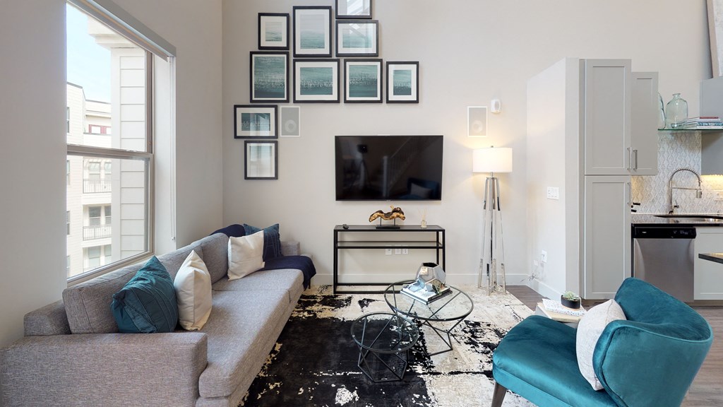 Living room area facing a couch next to an exterior window next to the kitchen