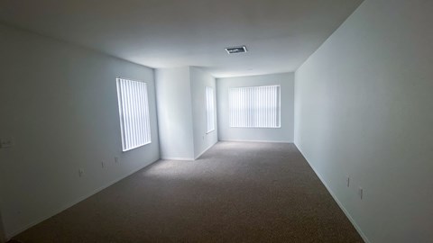 A spacious room with carpeted floor and two windows.