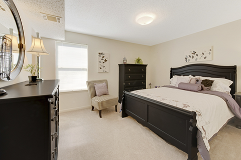 A bedroom with a large bed and a chair by the window.