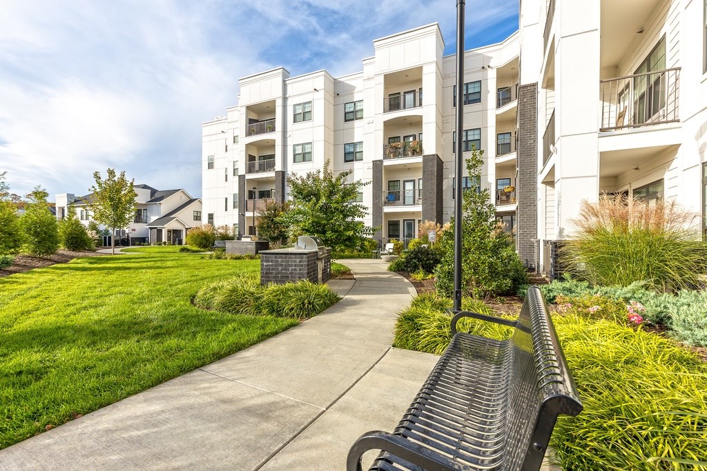A black bench is on a concrete path in front of a white apartment building.