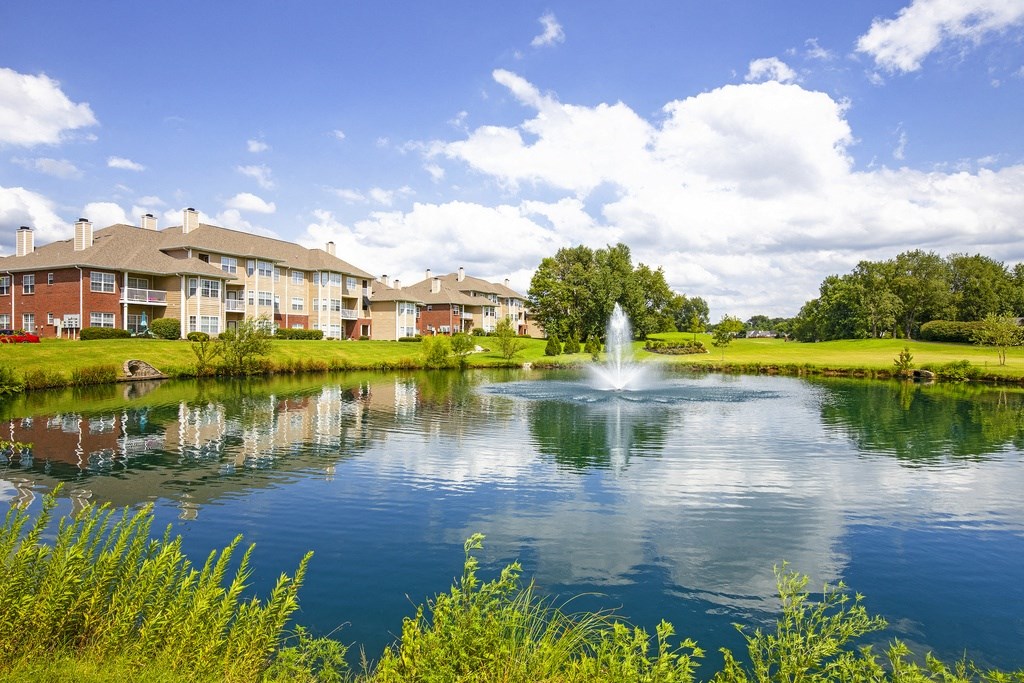 a fountain sits in the middle of a pond in front of apartment buildings