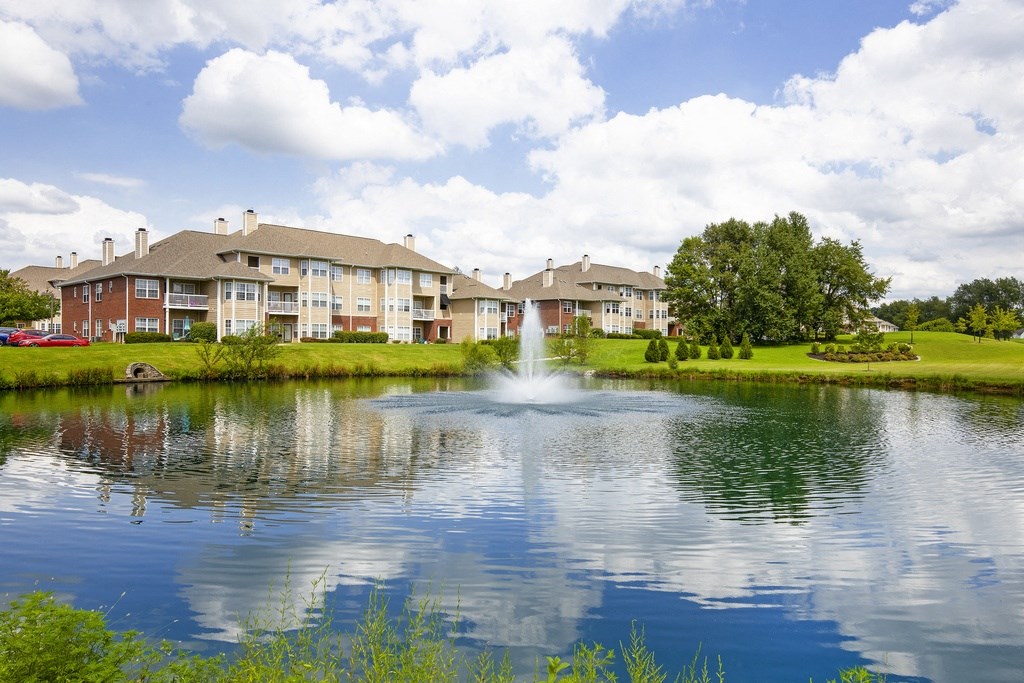 a fountain in the center of a lake with apartments in the background