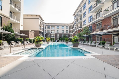 A large swimming pool surrounded by lounge chairs and umbrellas in a courtyard.