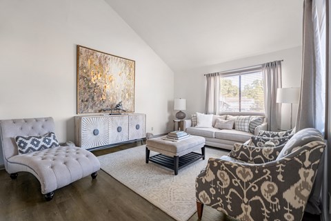 A living room with a grey sofa, a white chair, and a large painting on the wall.
