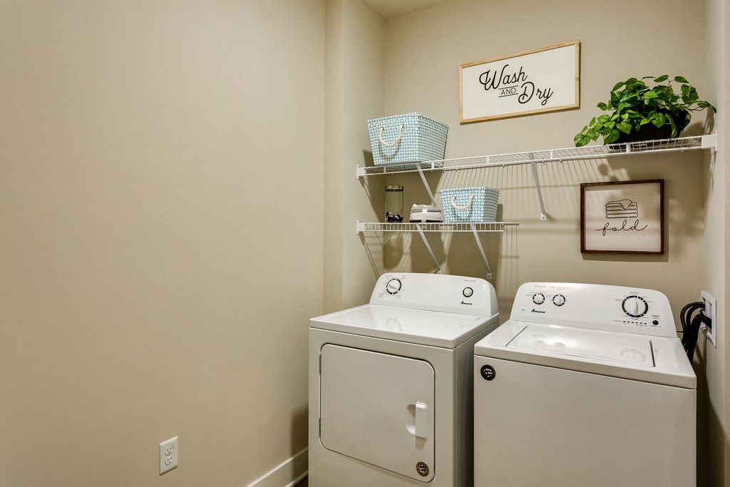 a laundry room with two washers and a dryer and a shelf with plants