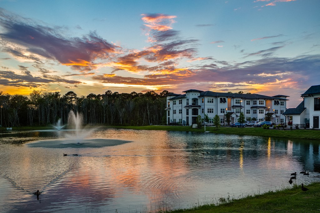 a sunset over a pond with a fountain in the middle of it