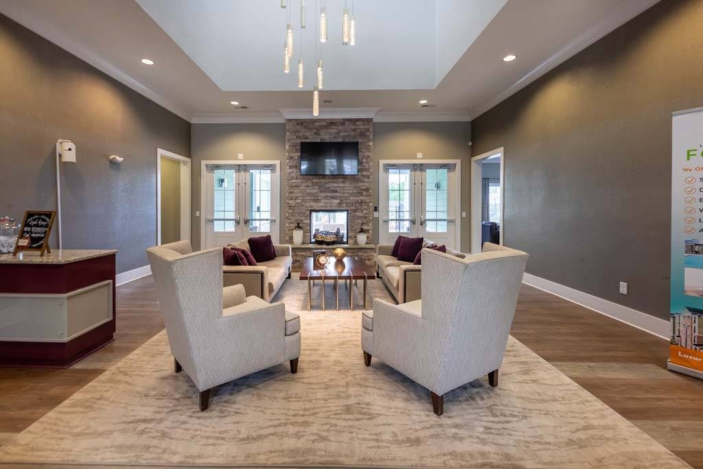 Two white chairs are placed on a rug in a room with a stone fireplace at Foxwood Apartments, Raleigh-Durham, North Carolina