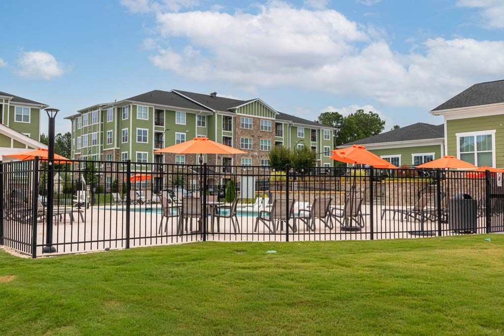 A black fence surrounds a pool area with orange umbrellas at Foxwood Apartments, Raleigh-Durham, NC, 27616