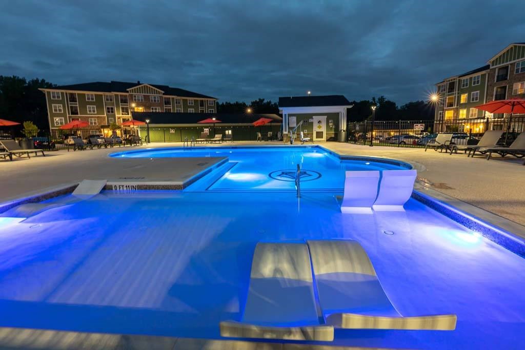 A large outdoor swimming pool lit up with blue lights at night. at Foxwood Apartments, Raleigh-Durham