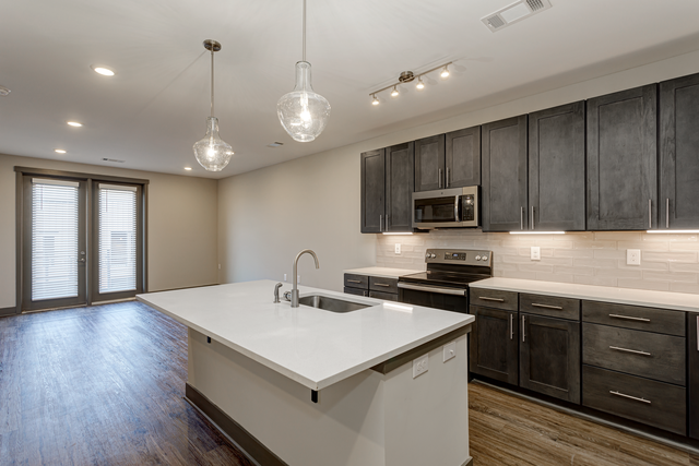 an empty kitchen with a white counter top and dark cabinets