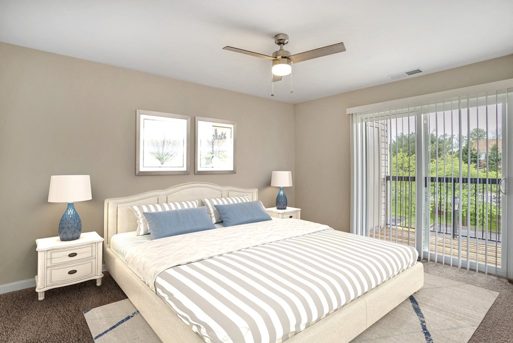 A virtually staged bedroom with gray walls with white trim, dark gray carpet throughout, and sliding glass door with vertical blinds leading to the outside patio/balcony area.