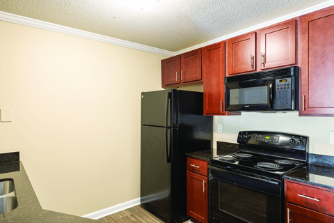 A kitchen with red cabinets and black appliances.