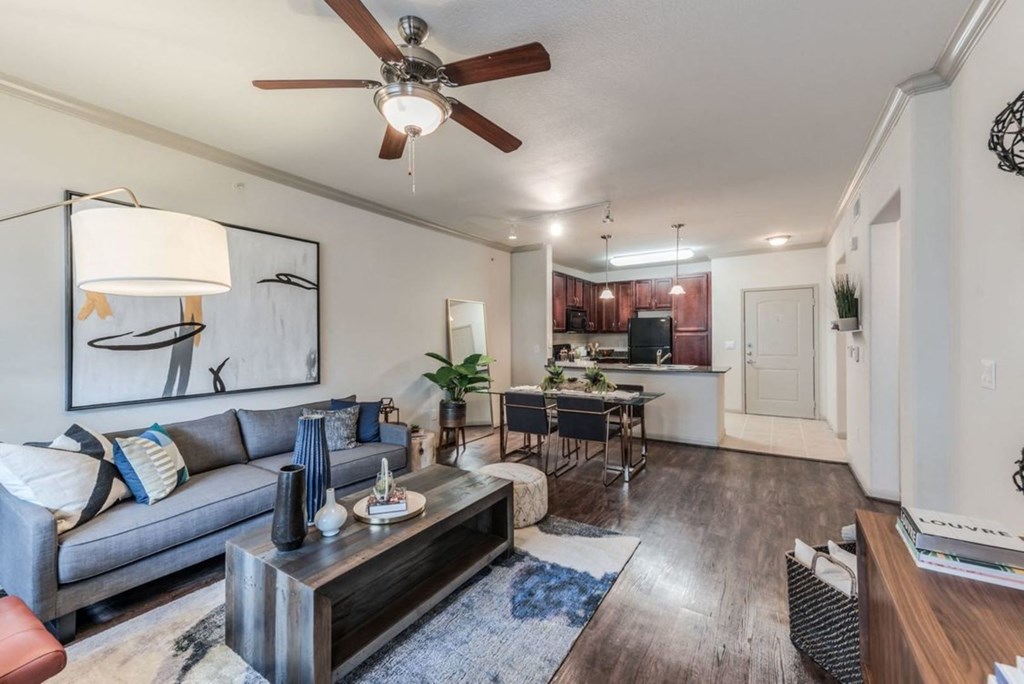a living room with a ceiling fan and a kitchen in the background