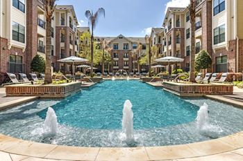a pool with water fountains and a brick building in the background