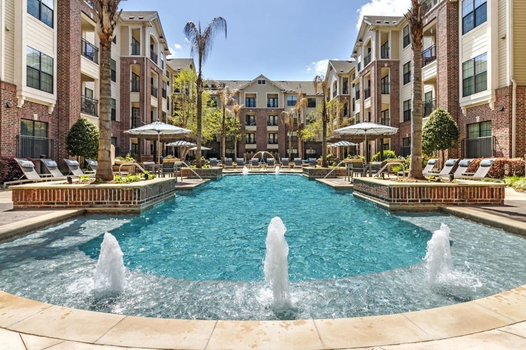 a pool with water fountains and a brick building in the background