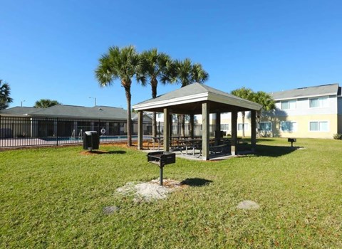 A gazebo sits in the middle of a grassy area with a building in the background.
