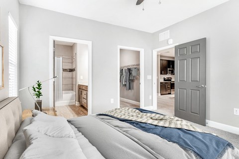 Vacant bedroom room with carpet with ceiling fan. Nightstands on side of the bed, art above the bed with view of bathroom and closet in the background.