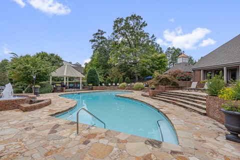A pool surrounded by a stone patio and a gazebo.