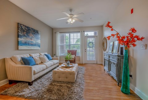 A living room with a beige couch, a brown rug, and a painting on the wall.