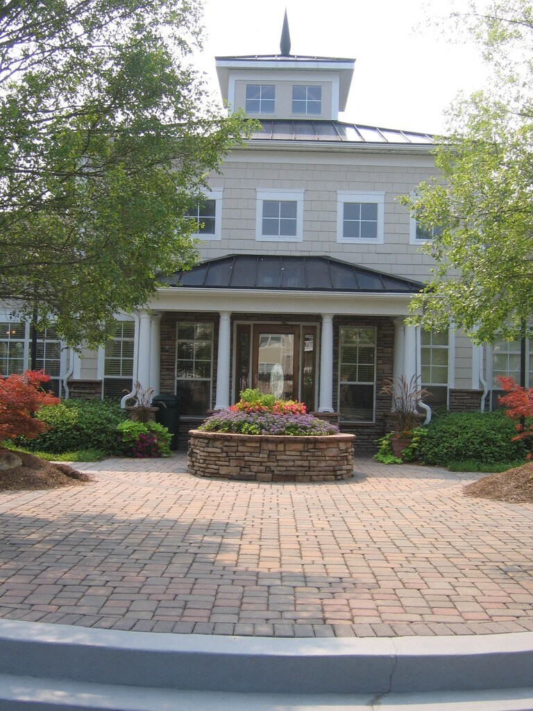 the front porch of a house with a brick walkway and a large flower garden