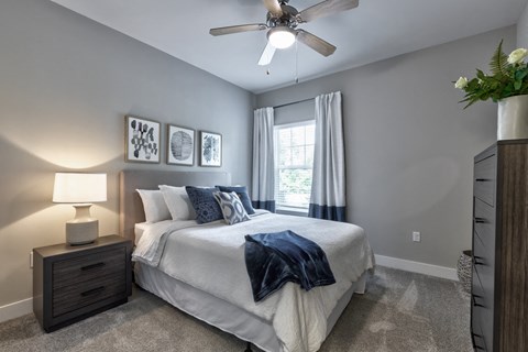 view of bedroom with ceiling fan and dresser and bed with white comforter