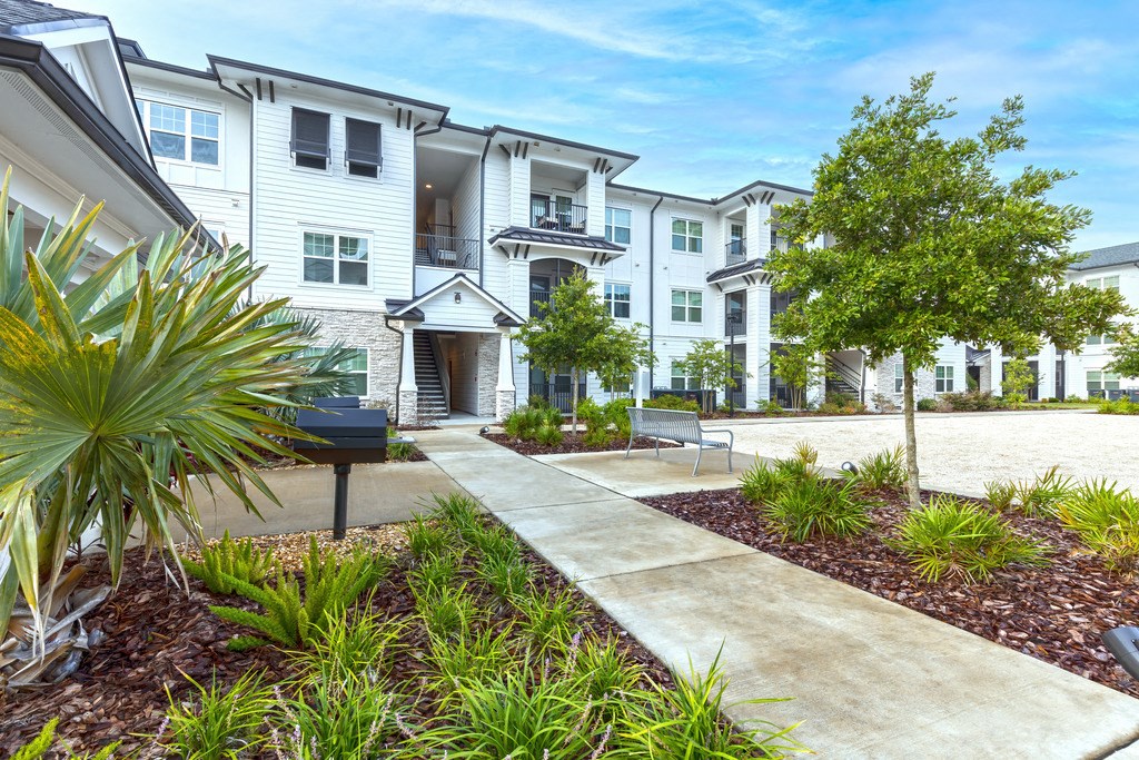 a sidewalk in front of an apartment building with trees and a grill
